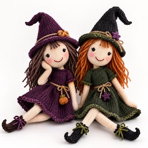 May include: Two knitted dolls dressed as witches. The left doll has brown hair, a purple dress, and a purple hat with a small pumpkin. The right doll has orange hair, a dark green dress, and a black hat with a small purple star. Both have rosy cheeks.