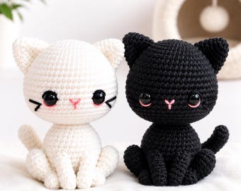 May include: Two handmade crochet cat dolls, one white and one black, featuring large glossy black eyes, small pink stitched noses, and embroidered whiskers. Each cat has a rounded head, pointed ears, and a seated posture with a visible tail.