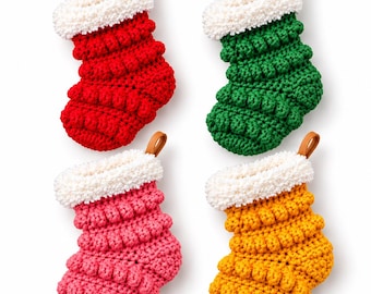 May include: Four crocheted stockings in red, green, pink, and yellow. Each stocking features a textured bobble stitch pattern, a white fuzzy cuff, and a small brown leather-like hanging loop at the top. The set displays four distinct colours.