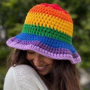 Può includere: Un cappello a secchiello all'uncinetto fatto a mano con un vivace motivo arcobaleno. Il cappello presenta fasce di rosso, arancione, giallo, verde, blu e viola. L'orlo è di una tonalità più chiara di viola. Un accessorio alla moda.