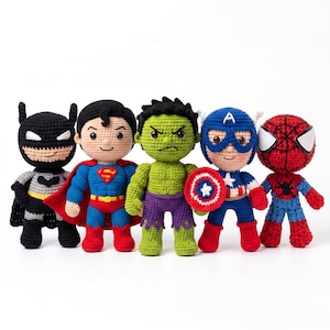 Puede incluir: Un conjunto de cinco muñecos de ganchillo que representan superhéroes. Las figuras incluyen a Batman en negro y gris, Superman con capa roja, un Hulk verde, el Capitán América con un escudo redondo y una figura de Spider-Man roja y azul.