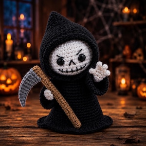 May include: A crocheted grim reaper doll featuring a white skull face with black stitched eyes and a mouth, wearing a black hooded robe. The figure holds a scythe with a brown handle and a grey blade, with one hand raised in a waving gesture.