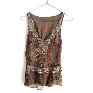 May include: A sleeveless brown top featuring a V-neckline, a paisley and animal print pattern, and intricate beadwork along the neckline and waist. The garment is constructed from a sheer, layered fabric and is displayed on a wire hanger.