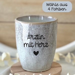 Könnte beinhalten: Ein gesprenkelter hellgrauer Keramikbecher mit dem schwarzen Schriftzug "Ärztin mit Herz" über einem kleinen schwarzen Herzsymbol. Ein hellgraues rechteckiges Etikett oben rechts enthält den schwarzen Text "Wähle aus 4 Farben".