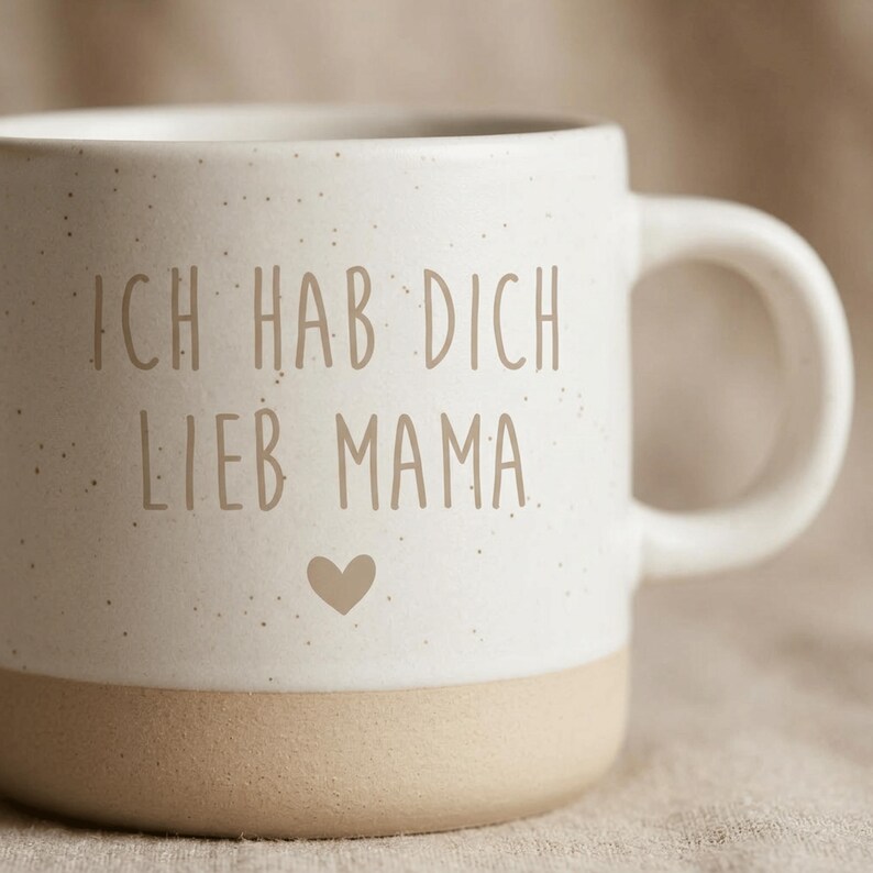 Op de afbeelding: Cr&egrave;mekleurige keramische mok met de Duitse tekst "ICH HAB DICH LIEB MAMA" in bruine letters en een hartje. De onderkant van de mok is lichtbruin en het handvat is wit.