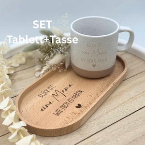 May include: A set including a speckled white mug with a tan base and a wooden serving tray. The mug and tray have German text and a heart symbol. The tray is oval-shaped and made of light-colored wood. The text on the mug and tray reads "Gl&uuml;ck ist eine Mama wie dich zu haben!"
