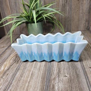 May include: A rectangular ceramic planter featuring a distinct zig-zag or accordion-pleated edge design. The exterior displays a gradient colour scheme, transitioning from a deep sky blue at the base to a crisp white finish along the top rim.