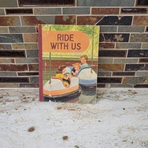 May include: A vintage children's book titled "Ride With Us." The cover features an illustration of children in bumper cars. The book has an orange and green cover with the title in large, bold letters. The book's spine is red.
