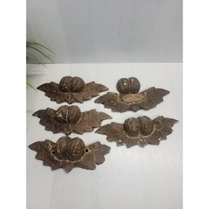 May include: Five antique-style drawer pulls. Each pull features a central, rounded knob atop a stylized leaf design. The pulls are finished in a distressed, dark brown color, suggesting an aged appearance. The pulls are made of a hard material.