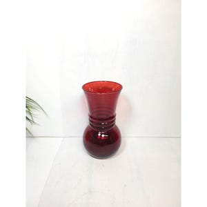 May include: A translucent ruby red glass vase featuring a bulbous base and a flared rim. The neck of the vase is decorated with three distinct horizontal rings molded into the glass, creating a textured appearance on the smooth, glossy surface.