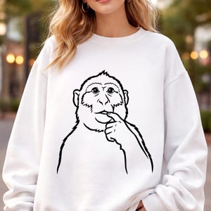 May include: White sweatshirt with a black and white monkey illustration. The design shows a monkey with its finger to its mouth. The sweatshirt has a crew neck and long sleeves. The illustration is on the front.