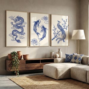 Peut inclure: Trois impressions d'art encadrées avec des illustrations bleues et blanches. Les impressions représentent un dragon, des carpes koï et un oiseau sur une branche fleurie. L'œuvre est exposée au-dessus d'un meuble TV en bois dans un salon.