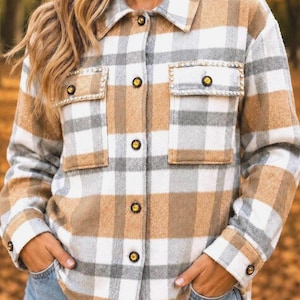 May include: A long-sleeved button-down shirt featuring a plaid pattern in tan, white, and gray. The shirt includes a classic collar, two chest pockets with decorative rhinestone trim, and dark buttons centered along the front placket and cuffs.