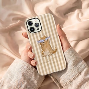 May include: A phone case with a vertical striped pattern in beige and white. The case features a cartoon illustration of a ginger cat holding two fish. The text at the bottom reads: "From blood moon on..."