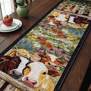 May include: A rectangular table runner featuring a colorful cow and floral design. The runner showcases a field of wildflowers with cows peeking over a wooden fence. The cows are in shades of brown, white, and yellow. The flowers are red, purple, and blue.