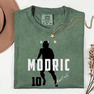 a green t-shirt with a silhouette of a person and the text "MODRIC 10" printed on it.