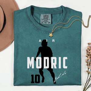 a green t-shirt with a silhouette of a person and the text "MODRIC 10" printed on it.