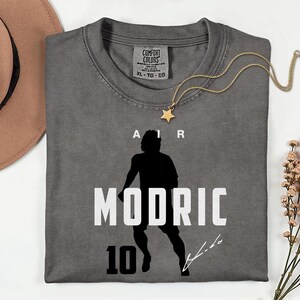 a gray t-shirt with a silhouette of a person and the text "AIR MODRIC 10" printed on it.