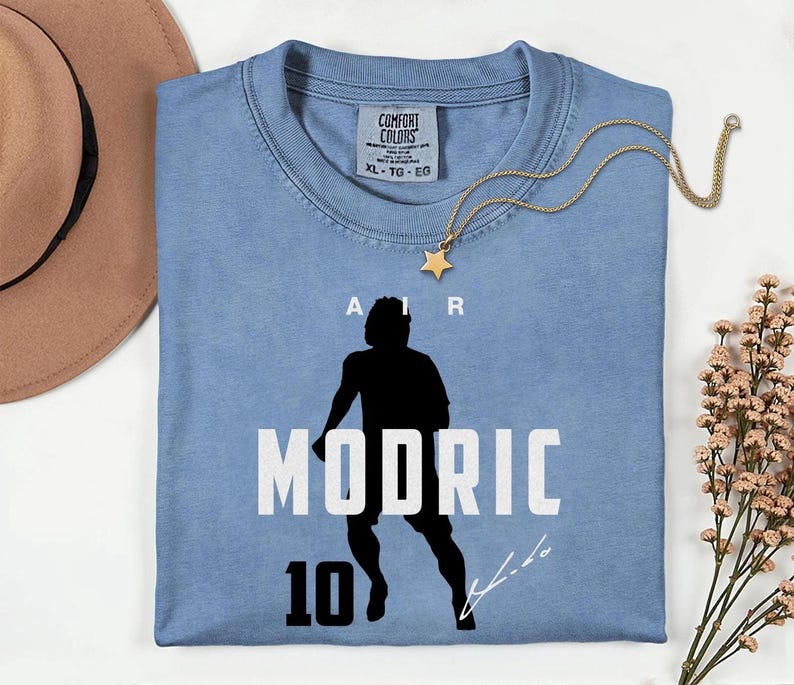 A blue t-shirt with a silhouette of a person and the text "MODRIC 10" printed on it, along with a gold star charm.