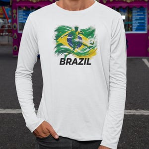 A white long-sleeved t-shirt with a graphic design depicting a soccer player in the Brazilian flag colors.