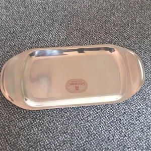 Könnte beinhalten: Ein Serviertablett aus Edelstahl mit abgerundeten Kanten. Das Tablett hat eine rechteckige Form mit einer polierten, reflektierenden Oberfläche. Der Markenname "Cromargan" ist auf dem Tablett sichtbar.