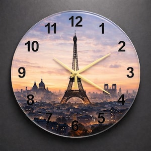 May include: Round wall clock featuring a scenic view of Paris, France, with the Eiffel Tower as the focal point. The clock face displays black numerals and gold-colored hands against a sunset sky. The clock is a decorative item.