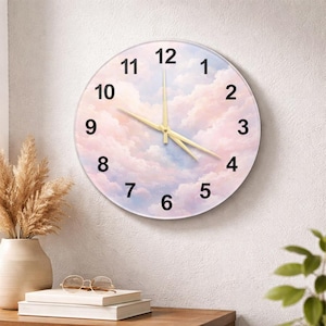 May include: A round wall clock with a pastel cloud design. The clock face features black numerals and gold-colored hands. The background is a soft blend of pink, blue, and white, resembling a dreamy sky. The clock is hanging on a white wall.