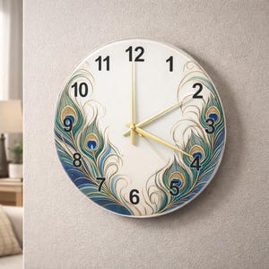May include: Round wall clock with a white face, gold hands, and black numerals. The clock features a peacock feather design in shades of blue, green, and gold. The clock is mounted on a light gray wall.