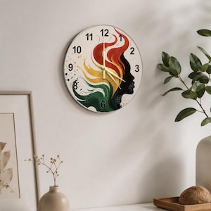 Puede incluir: Un reloj de pared redondo con la silueta de perfil de una persona con cabello fluido en tonos rojo, amarillo y verde. La esfera tiene números negros del 1 al 12 y manecillas delgadas de color dorado sobre un fondo de color crema claro.
