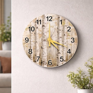 Op de afbeelding: Ronde wandklok met een berkenbosontwerp. De wijzerplaat toont zwarte cijfers en gele wijzers. De klok is aan een witte muur bevestigd, met een kleine plant rechtsonder.