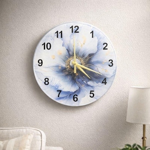Può includere: Orologio da parete rotondo con quadrante bianco e design floreale blu. L'orologio presenta numeri neri e lancette gialle. L'orologio è montato su una parete bianca strutturata.