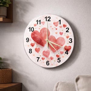 Może przedstawiać: Okrągły zegar ścienny z białą tarczą z dwoma dużymi akwarelowymi sercami i mniejszymi sercami w odcieniach czerwieni. Złote akcenty i czarne cyfry oznaczają godziny. Wskazówki zegara są jasnożółte.