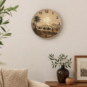 May include: Round wall clock with a desert scene featuring camels, a palm tree, and a sun. The clock face has black numerals and gold hands. The clock is mounted on a beige wall.
