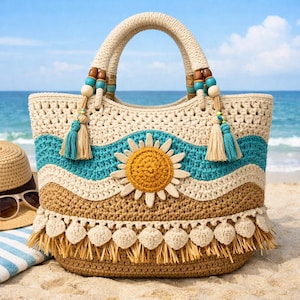 Könnte beinhalten: Eine cremefarbene, blaue und braune Häkeltasche mit einem Sonnendesign. Die Tasche hat einen cremefarbenen Griff mit Holzperlen und Quasten. Die Tasche ist mit einer Sonnenapplikation und Fransen am unteren Rand verziert. Ein Strohhut und eine Sonnenbrille sind im Hintergrund zu sehen.