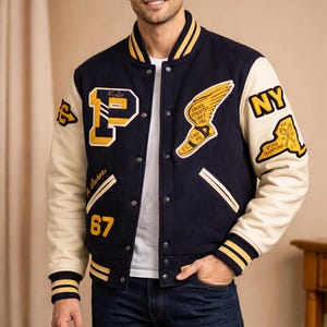 May include: Navy blue and cream varsity jacket with yellow accents and patches. Features a large "P" patch, "NY" patch, and other athletic-themed emblems. The jacket has a button-up front and striped cuffs.