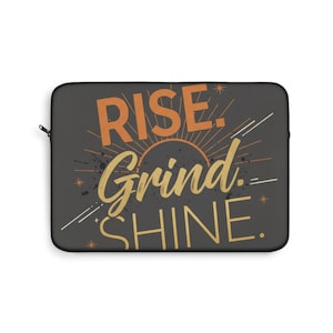 May include: A black laptop sleeve with the words "RISE. Grind. SHINE." in orange and gold lettering. The design includes a sunburst and star accents. The sleeve has a zipper closure.