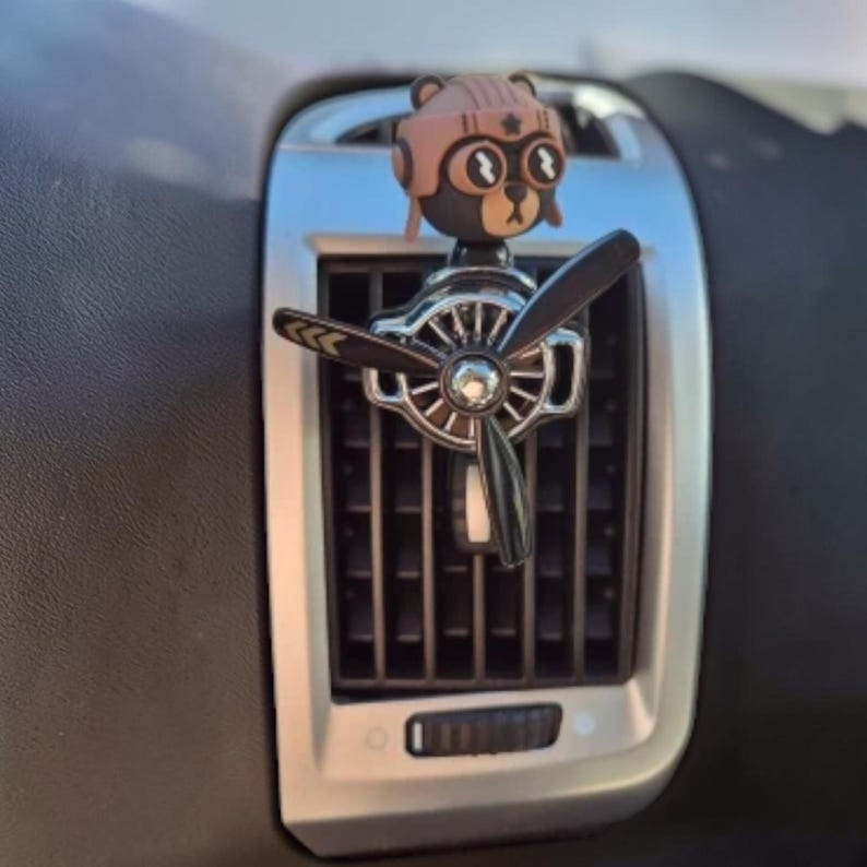 Airplane car air freshener with rotating propeller and pilot bear design, designed as a vent clip diffuser for car interiors. This decorative car accessory provides light fragrance while adding a fun aviation-inspired touch. Made from durable ABS material, it easily attaches to air vents and spins with airflow. Perfect for enhancing car decor and keeping your vehicle fresh during daily drives or road trips.