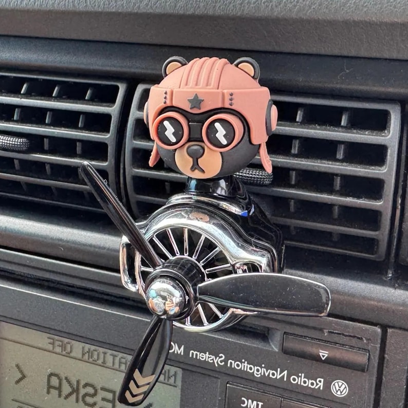 Airplane car air freshener with rotating propeller and pilot bear design, designed as a vent clip diffuser for car interiors. This decorative car accessory provides light fragrance while adding a fun aviation-inspired touch. Made from durable ABS material, it easily attaches to air vents and spins with airflow. Perfect for enhancing car decor and keeping your vehicle fresh during daily drives or road trips.