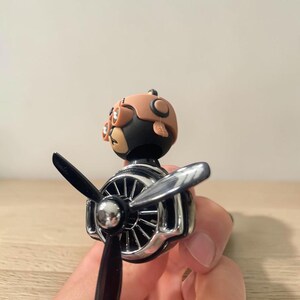 Airplane car air freshener with rotating propeller and pilot bear design, designed as a vent clip diffuser for car interiors. This decorative car accessory provides light fragrance while adding a fun aviation-inspired touch. Made from durable ABS material, it easily attaches to air vents and spins with airflow. Perfect for enhancing car decor and keeping your vehicle fresh during daily drives or road trips.