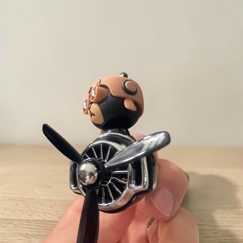 Airplane car air freshener with rotating propeller and pilot bear design, designed as a vent clip diffuser for car interiors. This decorative car accessory provides light fragrance while adding a fun aviation-inspired touch. Made from durable ABS material, it easily attaches to air vents and spins with airflow. Perfect for enhancing car decor and keeping your vehicle fresh during daily drives or road trips.