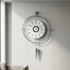 May include: A wall clock featuring a circular silver metal frame surrounding a white dial with black Arabic numerals. The centre of the dial has a black circular pattern with thin hands. A silver cone-shaped pendulum hangs from the bottom.