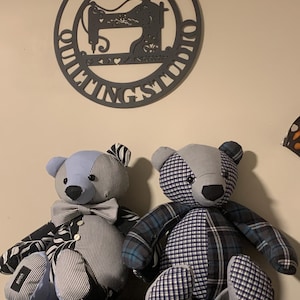 May include: Two patchwork teddy bears with different fabric patterns. One has a blue head and bow tie, the other a grey head. A sign above reads "Lori's Quilting Studio" with a sewing machine silhouette.