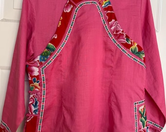 May include: A pink long-sleeved shirt with a mandarin collar. The shirt features a red floral pattern on the front, sleeves, and hem. The floral pattern includes pink, yellow, and blue flowers with green leaves.