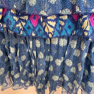 Puede incluir: Primer plano de una prenda fluida y escalonada en tonos azules. La tela presenta estampados florales y geom&eacute;tricos en azul claro, turquesa y magenta. Las capas crean un efecto de volantes, con una textura delicada y transparente.