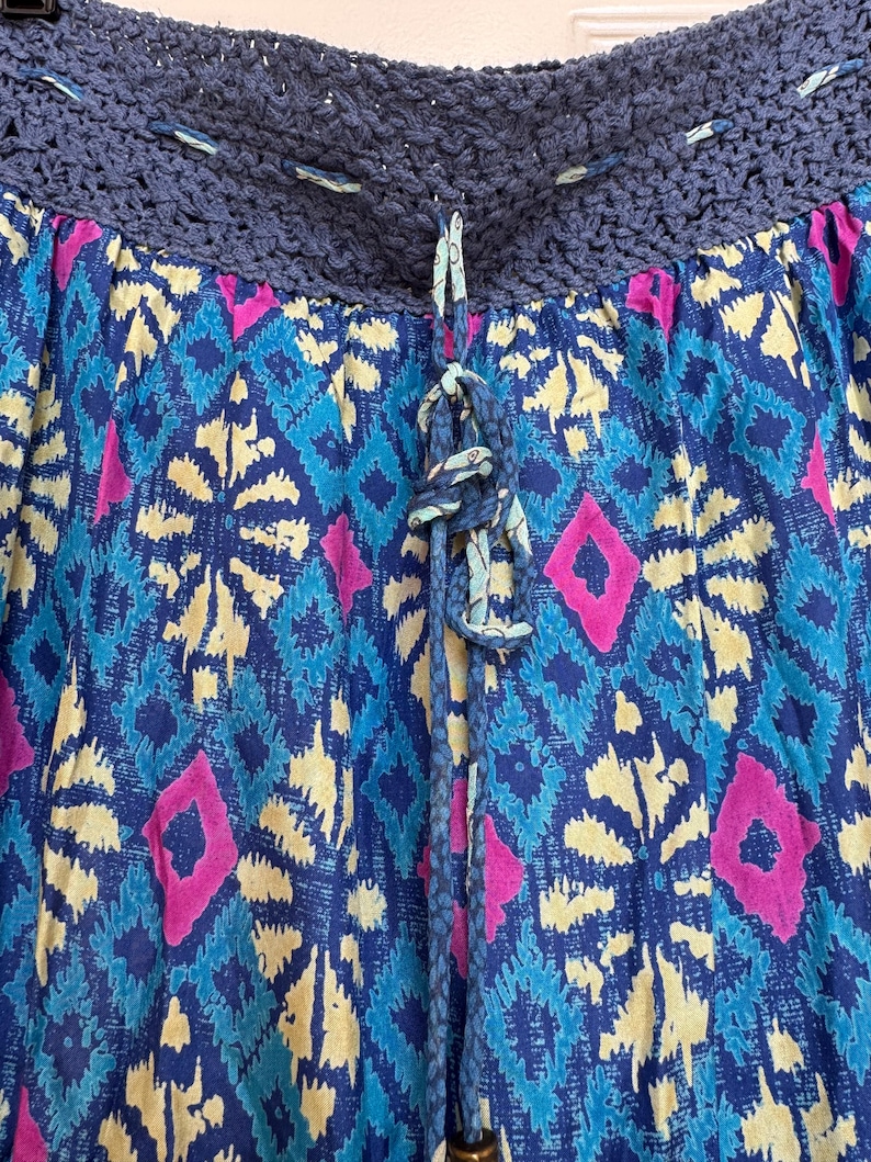 Puede incluir: Falda estampada con cinturilla de ganchillo y cord&oacute;n. La falda presenta un dise&ntilde;o vibrante de formas de diamante azules, amarillas y rosas. El cord&oacute;n es azul con un nudo decorativo.