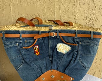 May include: A large straw tote bag with a denim front. The denim has a brown leather belt, two pockets, and patches that say "Kiss Me" and a cartoon cat. The bag has a brown leather handle.