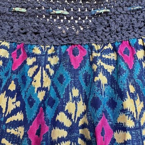 Puede incluir: Primer plano de una falda con una cintura de ganchillo azul marino y una tela estampada. La tela presenta un dise&ntilde;o vibrante con formas de diamantes azules, amarillos y rosas. El dise&ntilde;o de la falda es bohemio y colorido.