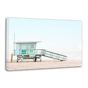 May include: A coastal print featuring a lifeguard station on a sandy beach. The light blue and green structure has a ramp and the number 42. The sky is a pale blue, and the overall aesthetic is minimalist.
