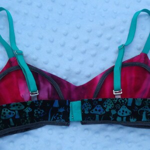 May include: A black and teal bra with a mushroom and floral print. The bra has adjustable straps and a hook and eye closure.