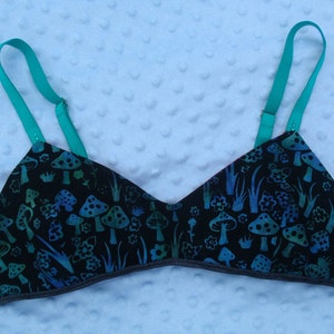 May include: A black bra with adjustable turquoise straps. The bra has a mushroom and grass print in shades of blue and green.